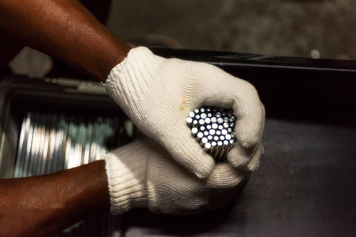 An employee's gloved hands lift freshly coated metal rods from the processor..